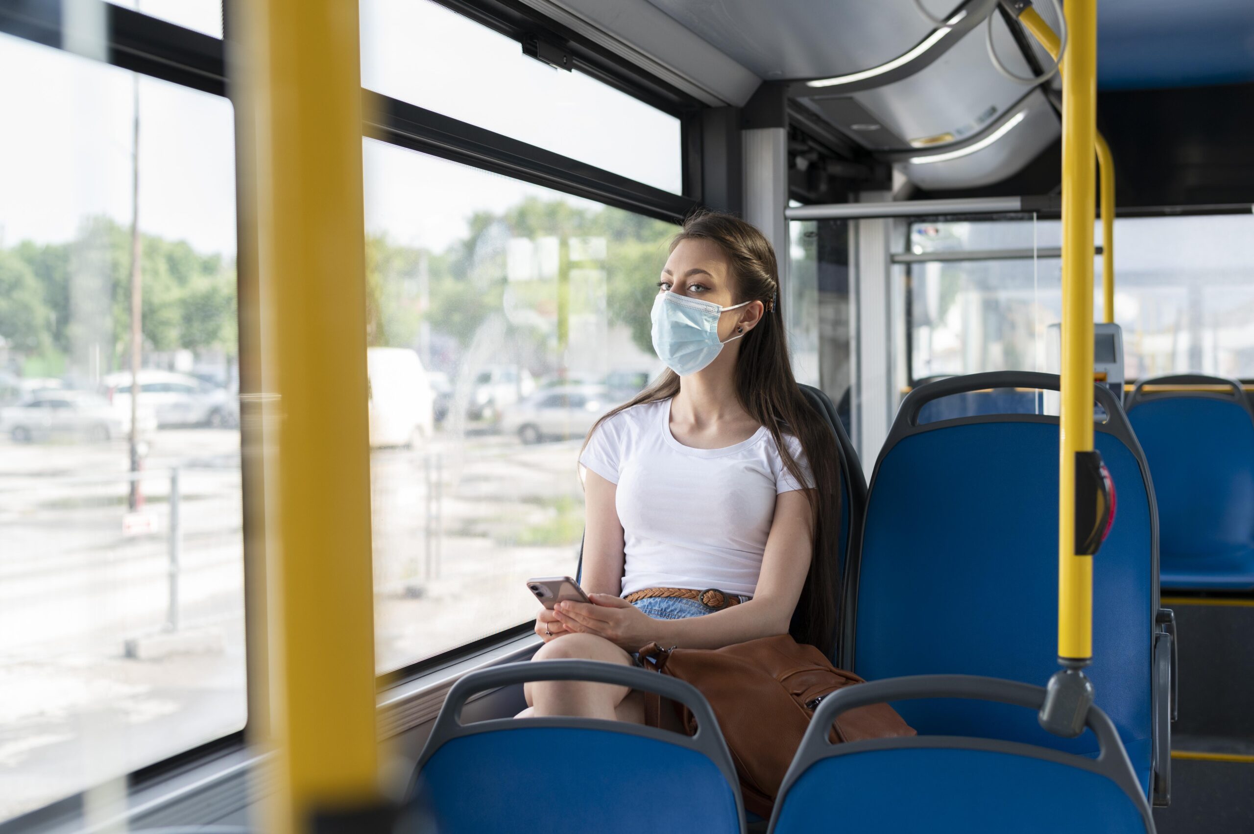 woman traveling by public bus using smartphone while wearing medical mask protection