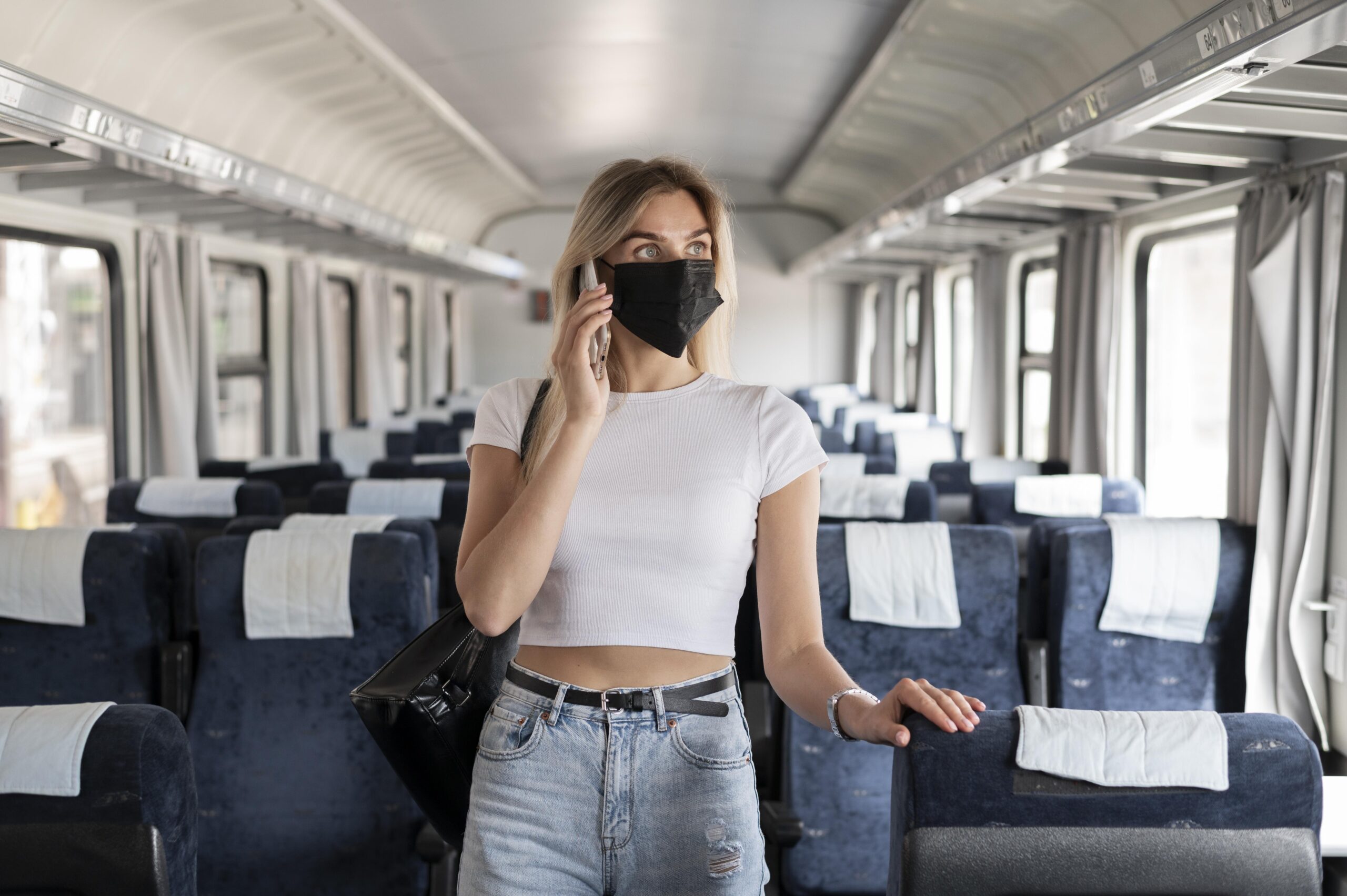 woman traveling by train talking phone while wearing medical mask